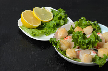 Fried scallop with boiled shrimp tail with lettuce leaves and lemon in a ceramic plate on a dark background.