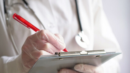 Close-up of a doctor writing a prescription in a medical record on a tablet. A doctor in a white coat and gloves is writing a prescription with a red pen. Medical banner concept,copy space