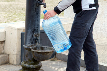 Riempire d'acqua un bottiglione in plastica dalla fontana pubblica. Sud Italia