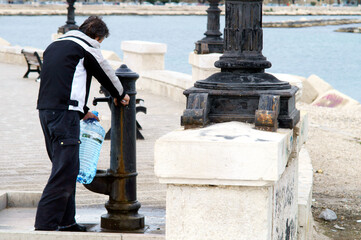 Riempire d'acqua un bottiglione in plastica dalla fontana pubblica. Sud Italia - obrazy, fototapety, plakaty