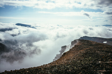 Atmospheric scenery on top of mountain ridge above clouds to vertex in thick low clouds. Minimalist view from precipice edge over clouds. Beautiful landscape with mountain range over dense clouds.