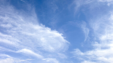 Panorama of white soft blurred clouds on a background of blue sky. Light clouds on a bright sunny summer day. The wind blows small clouds across the sky.