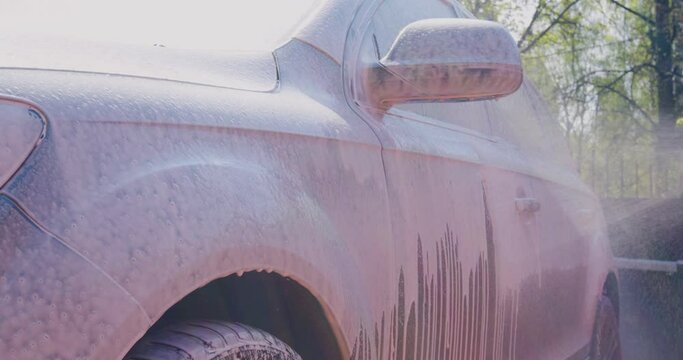 Close-up of covering car by soap foam on car exterior in car wash, auto service. Carwash, car detailing concept