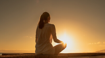 Young woman meditating by the sea at sunset. Being in a calm state of mind concept. 