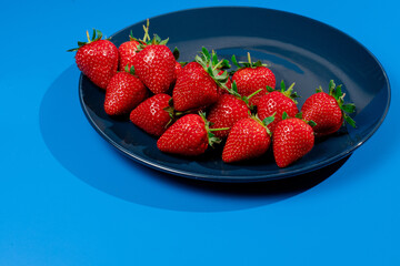Bunch of strawberry on plate on blue background. Summer seasonal red berry.