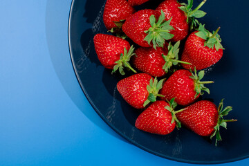 Bunch of strawberry on plate on blue background. Summer seasonal red berry.