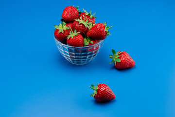 Bunch of strawberry in bowl on blue background. Yummy summer fruit.