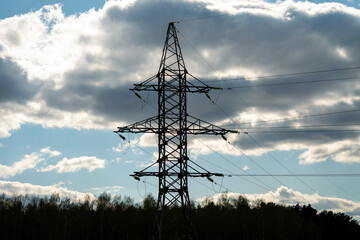 Silhouette of the power tower. High voltage electrical power line against blue sky with clouds