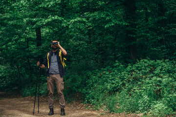 A hiker man walking in the forest using trekking poles and using binoculars