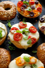 Baked bagels with cherry tomatoes, olives, mozzarella cheese and herbs on a dark background, focus on the sandwich inside  close up view