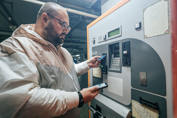 Man pays for underground parking in shopping mall automatic payment terminal using his phone or card.