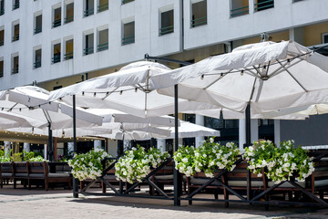 white sun umbrella over the tables with seating on the terrace of a street cafe decorated with...