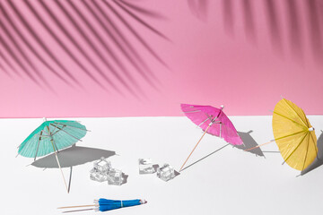 summer mockup with white and pink pastel colors. many beach or cocktail umbrellas and ice cubes at midday sun and hard shadows from palm leaves at the background for copy space