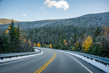 Winding highway between wooded mountains with evergreen and deciduous trees sprinkled with the...