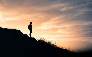 A woman standing at the top of the mountain and watching sunset