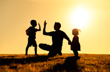 Fototapeta na wymiar Father interacting playing outdoors with his children giving high five. Parenting and fatherhood concept. 