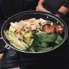 Korean pot with fried tofu, lettuce, mung bean, mushrooms, bok choy, and a girl