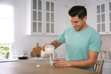 Man pouring milk from gallon bottle into glass at wooden table in kitchen