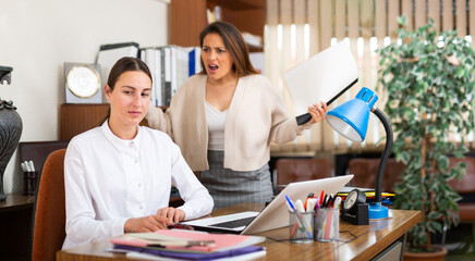 Angry business woman criticizing sad frustrated female employee sitting at office desk at work - obrazy, fototapety, plakaty