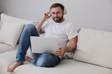 Man with laptop and headphones sitting on sofa at home
