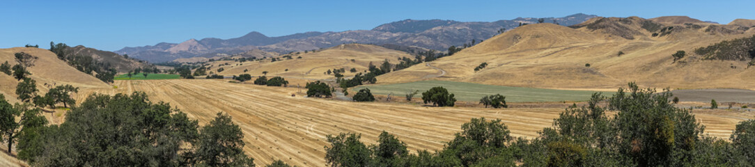 Fototapeta na wymiar Santa Inez, CA, USA - April 3, 2009: San Lorenzo Seminary. Panorama shot over yellow dry valley with freshly harvested hay bales, other green fields, mountains and blue sky.