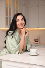 Pretty young woman wearing beautiful silk robe with cup of coffee in kitchen