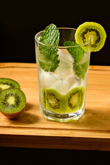 one glasses with iced drink decorated with kiwi mint and ice, on an insulated wooden board on a black background