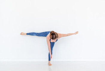 Young diverse woman practices yoga in a pose. Standing on the floor. White studio loft.