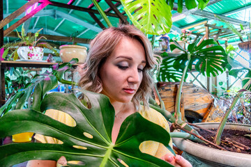 Young woman with blond hair stands in greenhouse and looks at plants. Natural nature. Wellness concept