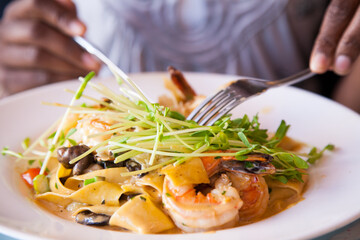 Hands holding knife and fork 
to eat plate of seafood with pasta 