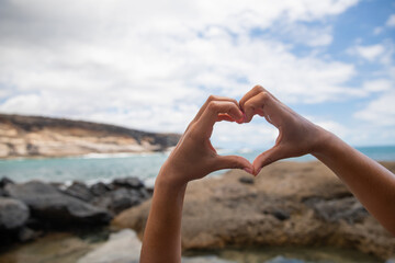 Close up og the Heart-shaped hands of a girl having fun and enjoying the summer at the beach. Love nature concept.