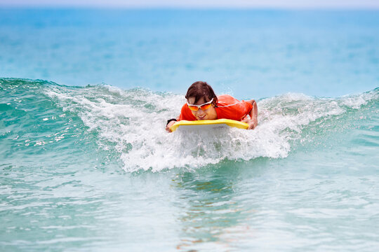 Child surfing on tropical beach. Surfer in ocean.