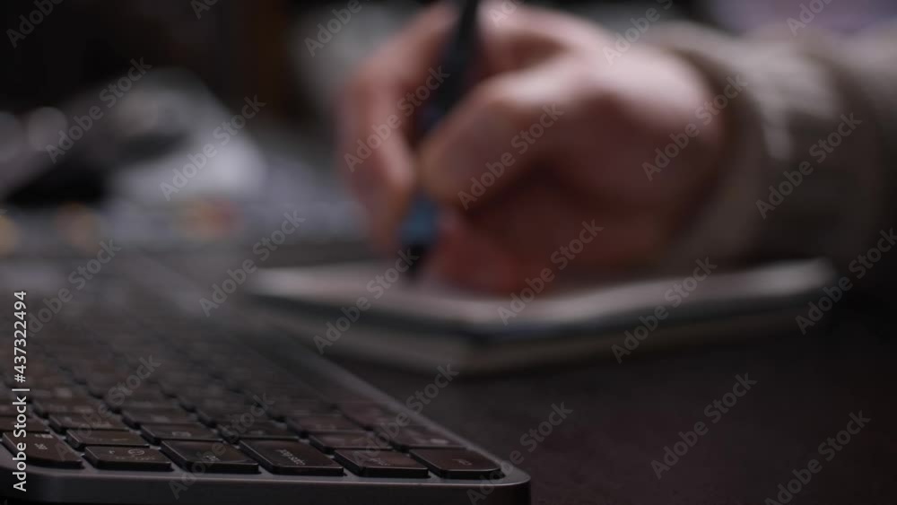Poster hand writing in notebook, keyboard from a side perspective with blurred background.