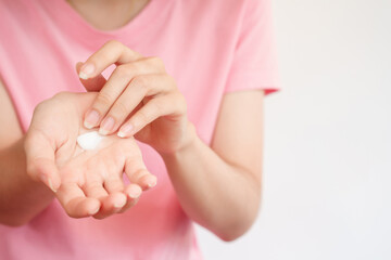 A woman in a pink dress is applying a moisturizer to keep her skin healthy. Body care ideas.