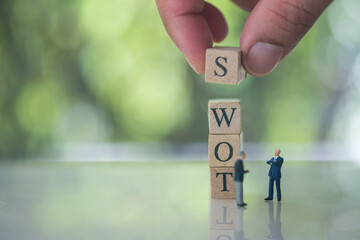 Hand putting wooden cube of S on W, O, T beside miniature people businessman meeting.