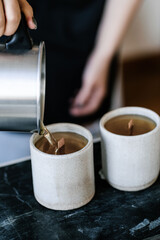 The girl pours wax into a gray concrete candle mold.