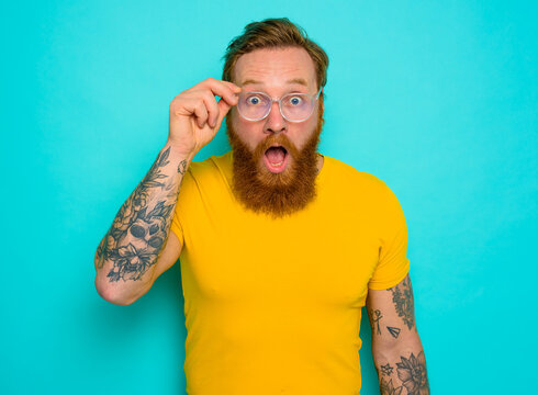 Man with yellow t-shirt and beard is shocked about something