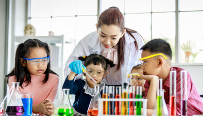 Asian little boy drop reagent sample by glass dropper into colorful solution flask while young...