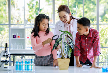 Asian female botany teacher in white lab coat teach botanical knowledge to primary boy and girl...