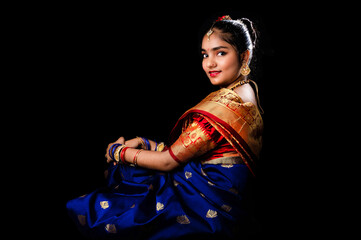 Beautiful Indian girl with clean healthy skin on black background. Wear red and blue Marathi saree.
