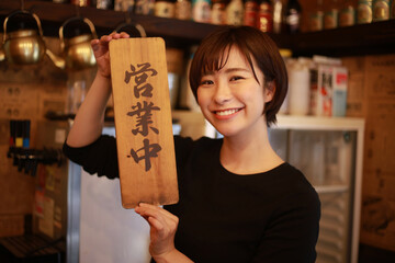「営業中」の看板を持つ女性店員