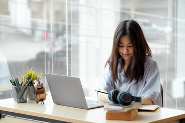 Online education. Asian girl with headphones makes an online lesson using a computer video call to a virtual teacher at home