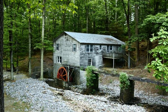 Old Mill House on stream with a red mill wheel in the forest on a warm spring day.