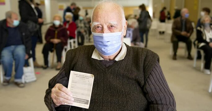 Tender grandpa  in a mask looks at the ID card. Vaccination Passport. Pfizer BioNTech COVID-19 Vaccine against Coronavirus.