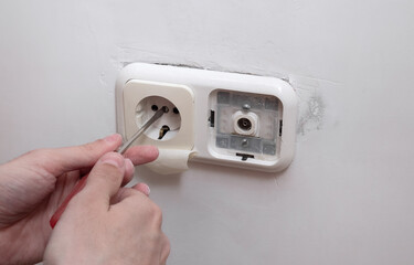 man works with electricity and installing new socket by using screwdriver. House renovation conception. repairman removes the socket before painting the walls