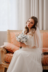 portrait of a beautiful bride with a bouquet on the couch. Wedding traditions.