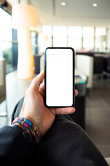 (Copy space) Overhead view of an human hand holding a smart phone with a white screen in an airport lounge. Concept of showing information on a mobile phone during Covid-19 pandemic.