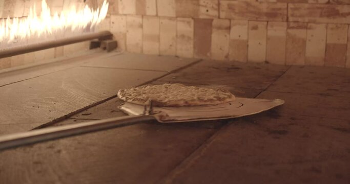 Pizza or Arabic manakish food being cooked and flipped inside a brick oven