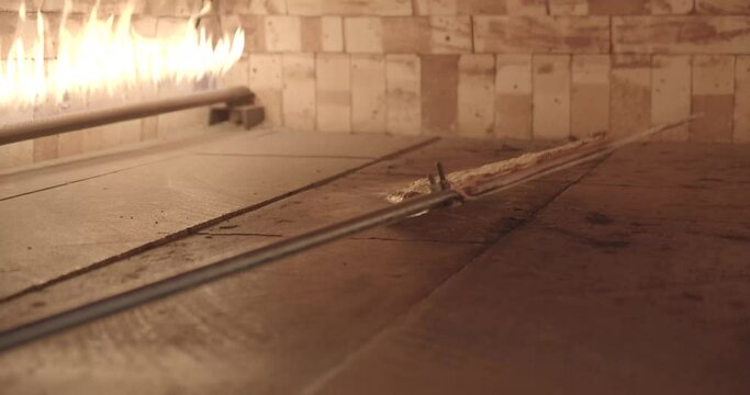 Pizza or Arabic manakish being cooked and pulled out of flame brick oven