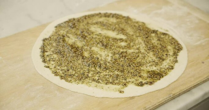 Green paste zaatar being spread on dough to make arabic manakish